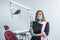 Beautiful female dentist standing in the dentistry near dental unit, holding medical tools and ready ready to accept a new patient