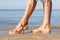 Beautiful female feet step on sea water along seashore with golden sand. Resting on the sea concept.