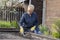Beautiful female gardener removes weeds from garden with hoe, cultivating soil