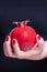 Beautiful female hand holding ceramic red pomegranate fruit. Manicure with red nail polish. Black background