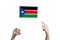 A beautiful female hand holds a South Sudan flag to which she shows the finger of her other hand, isolated on white background