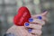 Beautiful female hand with manicure holds a plush heart. Bright blue nail polish.