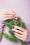 Beautiful female hands holding Christmas tree branch and vintage toy penguin on the pale violet background. Manicure