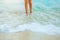 Beautiful female legs against the background of a breaking wave. Sea foam splash up. Paradise beaches, azure water