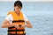 Beautiful female lifeguard putting on life vest near sea