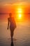 Beautiful female model open arms under sunrise at seaside. Calm water of salt lake Elton reflects woman silhouette. Sun goes