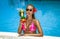 Beautiful female model in pink bikini is standing in the pool and holding colorful fruity drink. Sexy woman in sequin bikini is