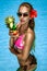 Beautiful female model in pink bikini is standing in the pool and holding colorful fruity drink. Sexy woman in sequin bikini is