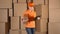 Beautiful female warehouse worker in orange uniform searching item against brown cardboard boxes backround. 4K video