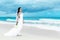 beautiful fiancee in white wedding dress with big long white train and with wedding bouquet stand on shore sea
