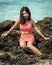 Beautiful Filipina in a red swimsuit smiling and posing at a beach on a rock with water in the back
