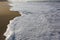 Beautiful filled frame close up seascape wallpaper background shot of golden orange sand with white foamy waves of the Indian