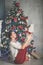 Beautiful flexible young woman is doing stretching exercise near decorated fashion xmas tree, sports and holiday concept