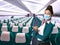 A beautiful flight attendant in a green jacket and mask in front of an airplane aisle. Subject on blurred background