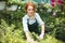 Beautiful florist in apron and pink gloves thoughtfully working with plants in greenhouse