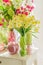 Beautiful flowers in green and pink vases, Candles and glass apples on white wooden  commode. Spring interior decoration