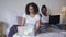 Beautiful focused African American young woman working online on laptop with man surfing Internet at background