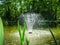 Beautiful fountain in garden pond against background of emerald green of shady summer garden. Freshness of water