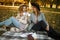 Beautiful friends spending time on a picnic blanket on the grass. Two young carefree smiling sisters making picnic eating fruits a