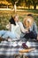 Beautiful friends spending time on a picnic blanket on the grass. Two young carefree smiling sisters making picnic eating fruits a