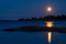 A beautiful full moon casting reflection on the calm water. A silhouette of a small skerry with a flock of Canada Gooses