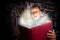 Beautiful funny child holding a big book with magical light looking amazed