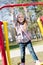 Beautiful funny cute little girl having fun riding a swing looking at camera & happy smiling in the park on spring or autumn