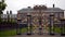 Beautiful gates with gold patterns. Action. Facade of old manor house with green lawn and black graceful gate in cloudy