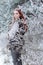Beautiful gentle girl with red hair in a fur vest standing in a snowy forest with iniem on the branches of trees