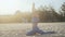 Beautiful gentle girl sitting in a yoga pose on a sandy beach in the early sunny morning in white socks