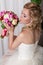 Beautiful gentle young girl happy bride in a white dress sitting on a chair and smelling a bridal bouquet with a nice manicure