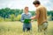 Beautiful girl agronomist with note book standing in wheat field and looking at crop in farmer man hands, green and yellow wheat