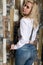 Beautiful girl with big boobs in a vintage blue jeans and white shirt poses near a wooden wall.