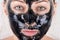 A beautiful girl with a black mask on her face is lying on a white soft towel very close-up. Black face mask with activated carbon