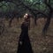 Beautiful girl in in black vintage dress with curly hair posing in the woods. Woman in retro dress lost in the forest. Worried sen