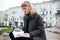 Beautiful girl with blond hair sitting with notebook in hand on city street