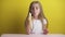 Beautiful girl with blond hair in a white T-shirt on a yellow background eats a banana and looks at it,