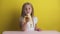 Beautiful girl with blond hair in a white T-shirt on a yellow background eats a banana and smiles. happy childhood,