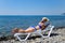 A beautiful girl in a blue bikini and a white hat is sunbathing on the beach, lying on a white chaise longue. Blonde
