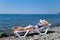 A beautiful girl in a blue bikini and a white hat is sunbathing on the beach, lying on a white chaise longue. The blonde