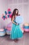 Beautiful girl in blue dress hold in hand huge candy in studio with decor of macaroons. Copy space.