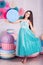 Beautiful girl in blue dress hold in hand huge candy in studio with decor of macaroons. Copy space.