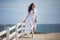 A beautiful girl, bride, in a white dress, barefoot, walking near a white fence, on a kiln beach.