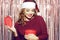 Beautiful girl in a bright santa hat is holding a red box with a gift for the new year. Christmas brunette in a red sweater