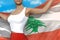 Beautiful girl in bright skirt holds Lebanon flag in hands behind her back on the cloudy sky background - flag concept 3d