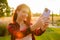 A beautiful girl captures selfie using a mobile photo in the field in a radiant sunbeam