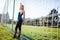 A beautiful girl with closed eyes in a blue shirt and leggings stands near a football goal at the stadium at sunset. Beautiful sun