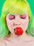 Beautiful girl with color hair holds strawberry with lips on green background