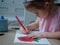 A beautiful girl in a crown 4-5 years old draws with multi-colored pencils in the coloring at home at the table