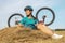 Beautiful girl cyclist sitting on dry grass on the background of the bike. Nature and man